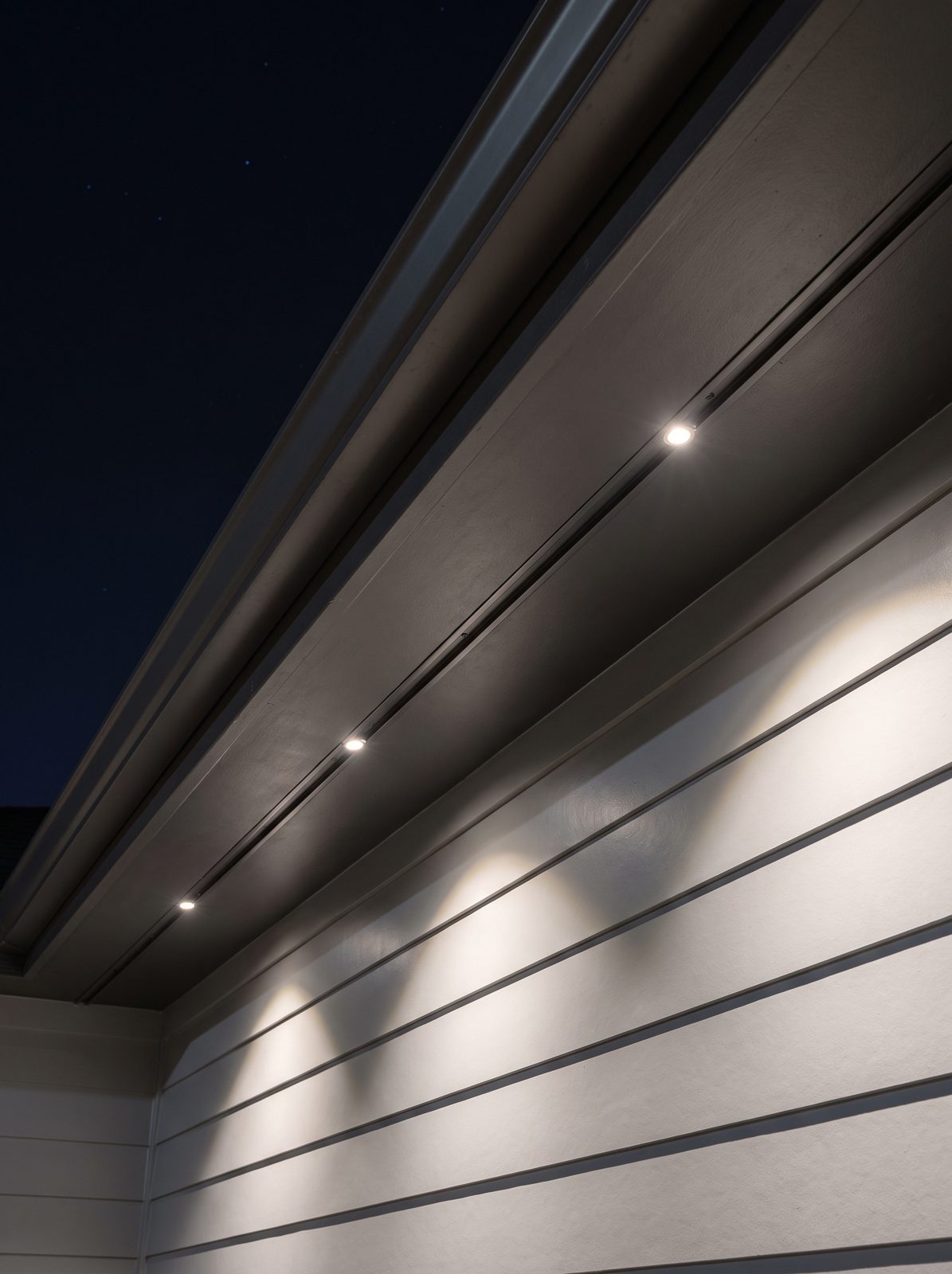 Warm white recessed lights installed in charcoal track beneath a home's eave